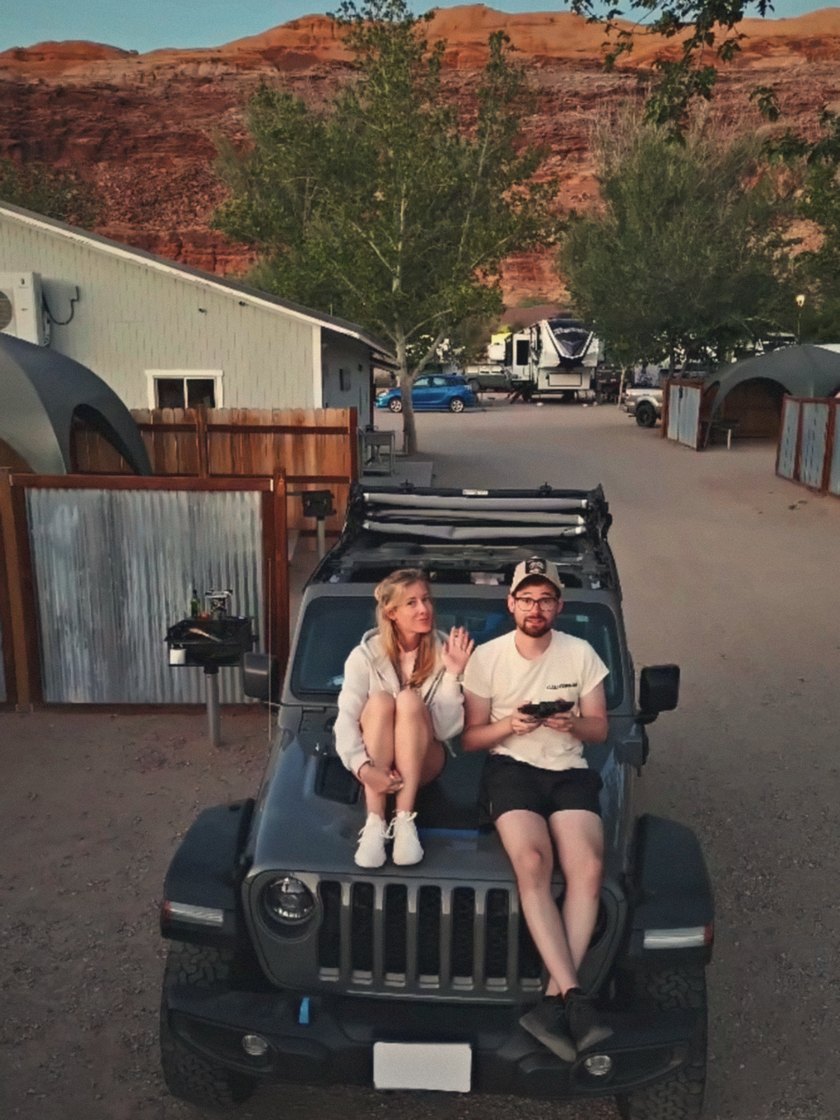 Florence and Simon sitting on the hood of an off-road car, red cliffs in the evening light behind them